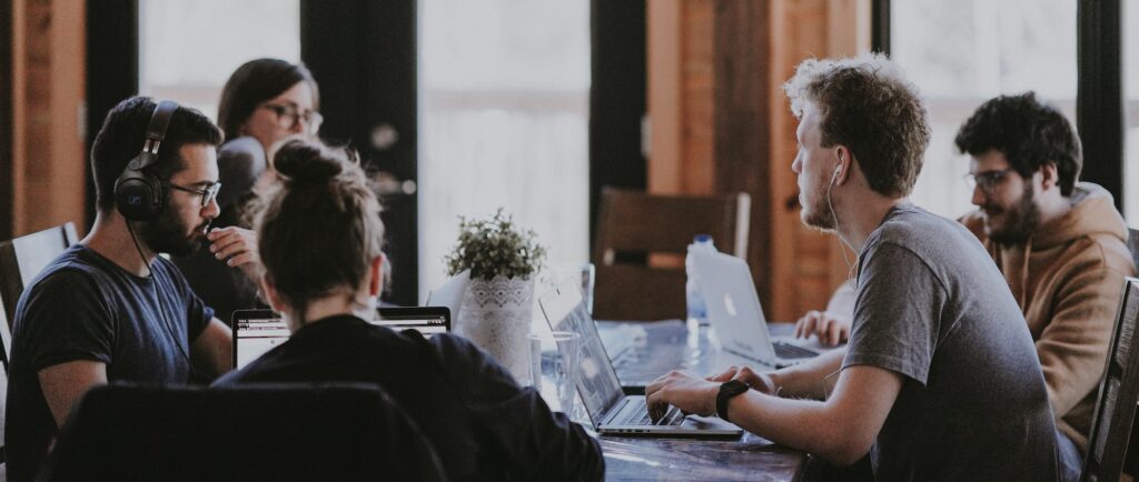 A group of people sitting around a table with laptops in front of them