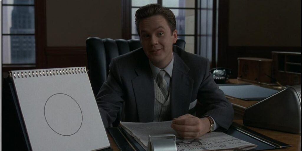 Tim Robbins in the Hudsucker Proxy sitting at his desk with the circle painting next to him